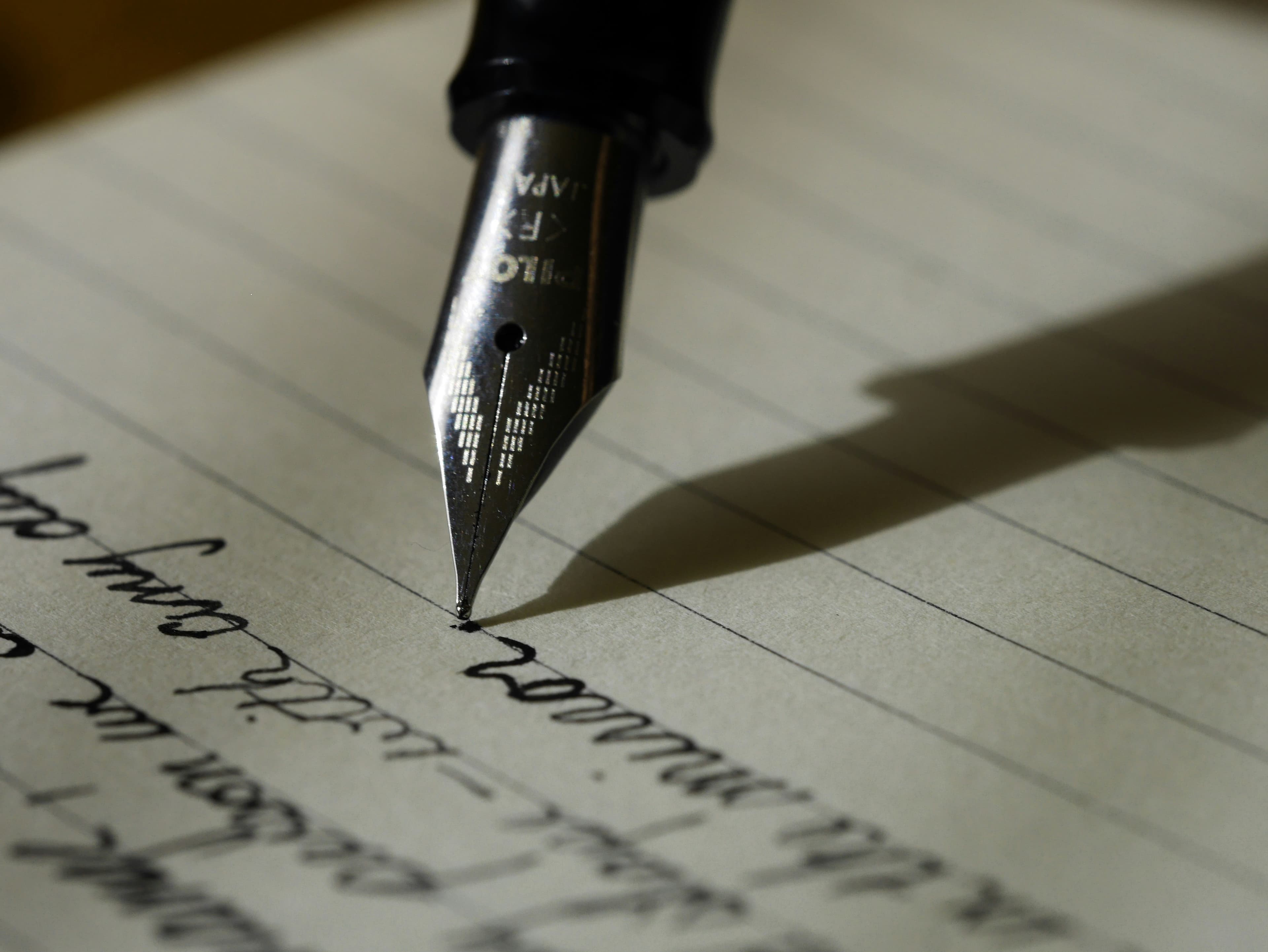 A hand writing with a fountain pen on paper, the kind of careful drafting a formal German letter asks for