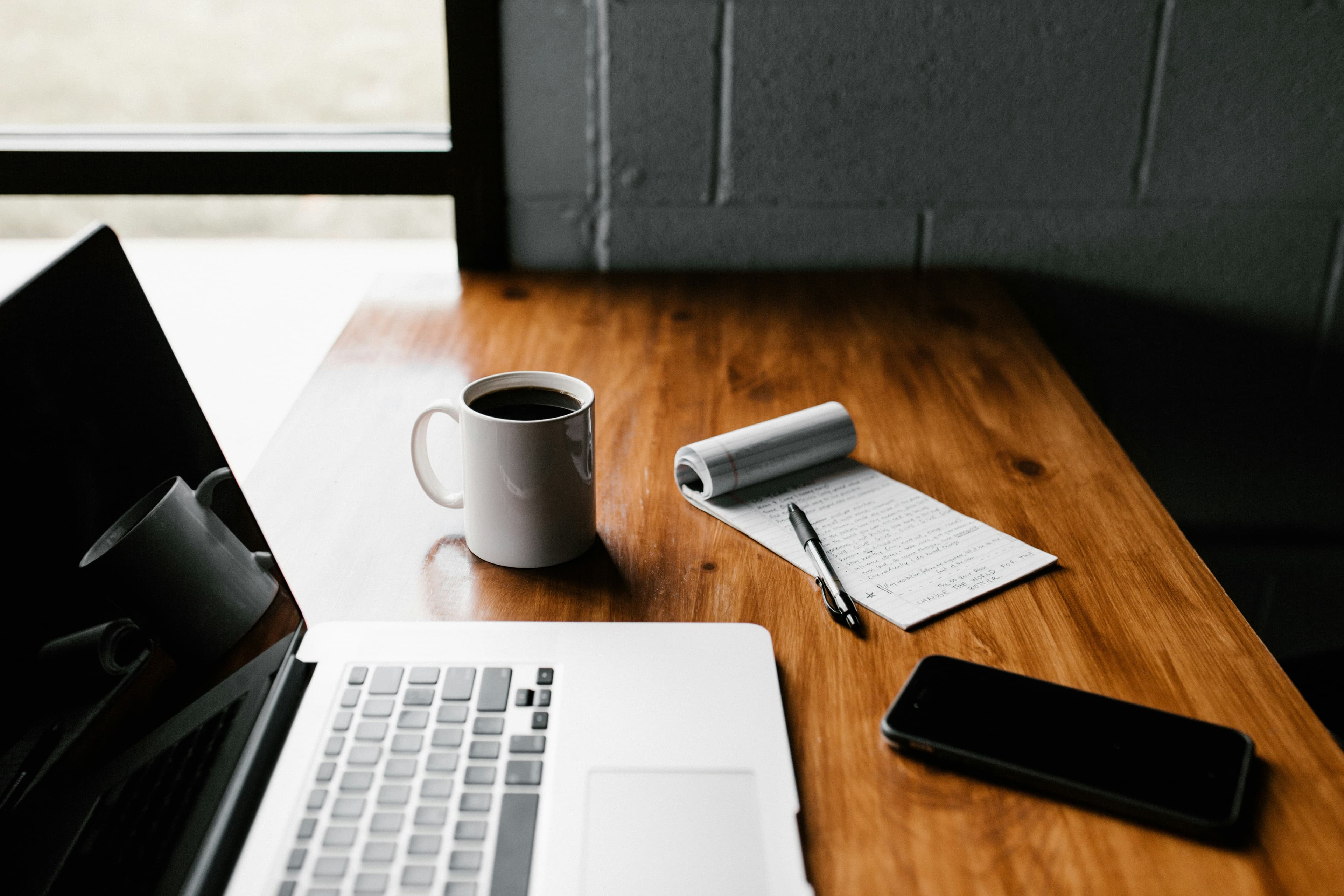 A laptop open on a wooden desk next to a notebook and pen, set up for self-paced online study
