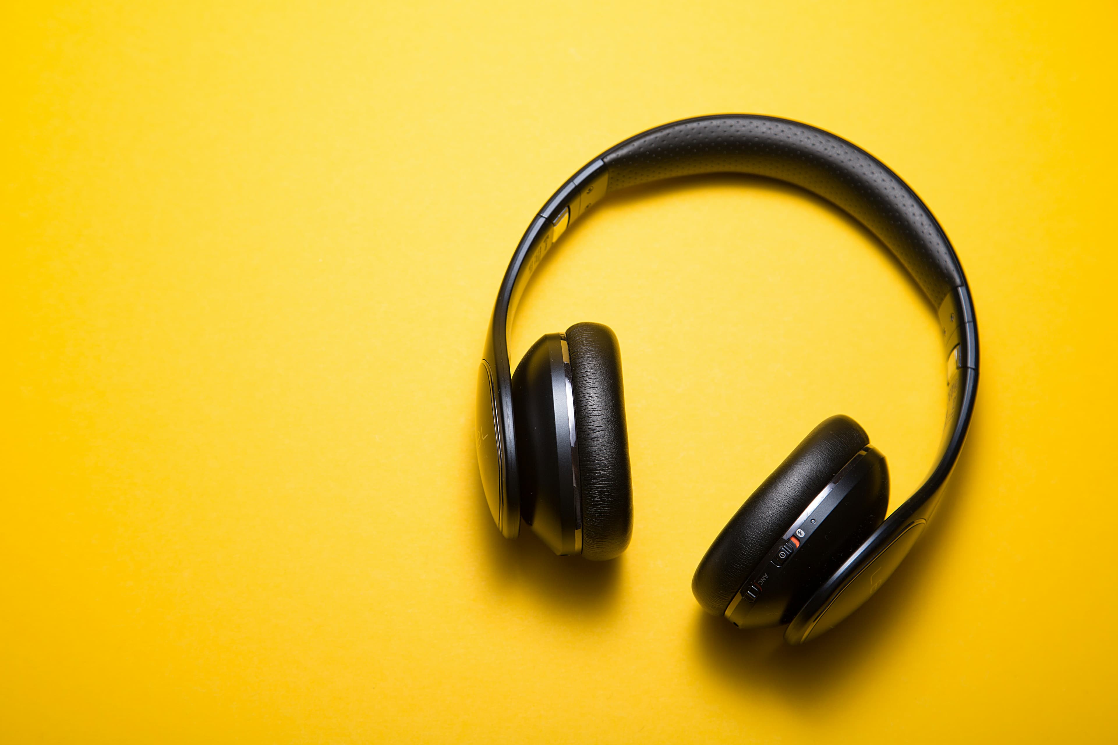 A pair of yellow over-ear headphones on a plain background, the kind you'd wear for focused German listening practice