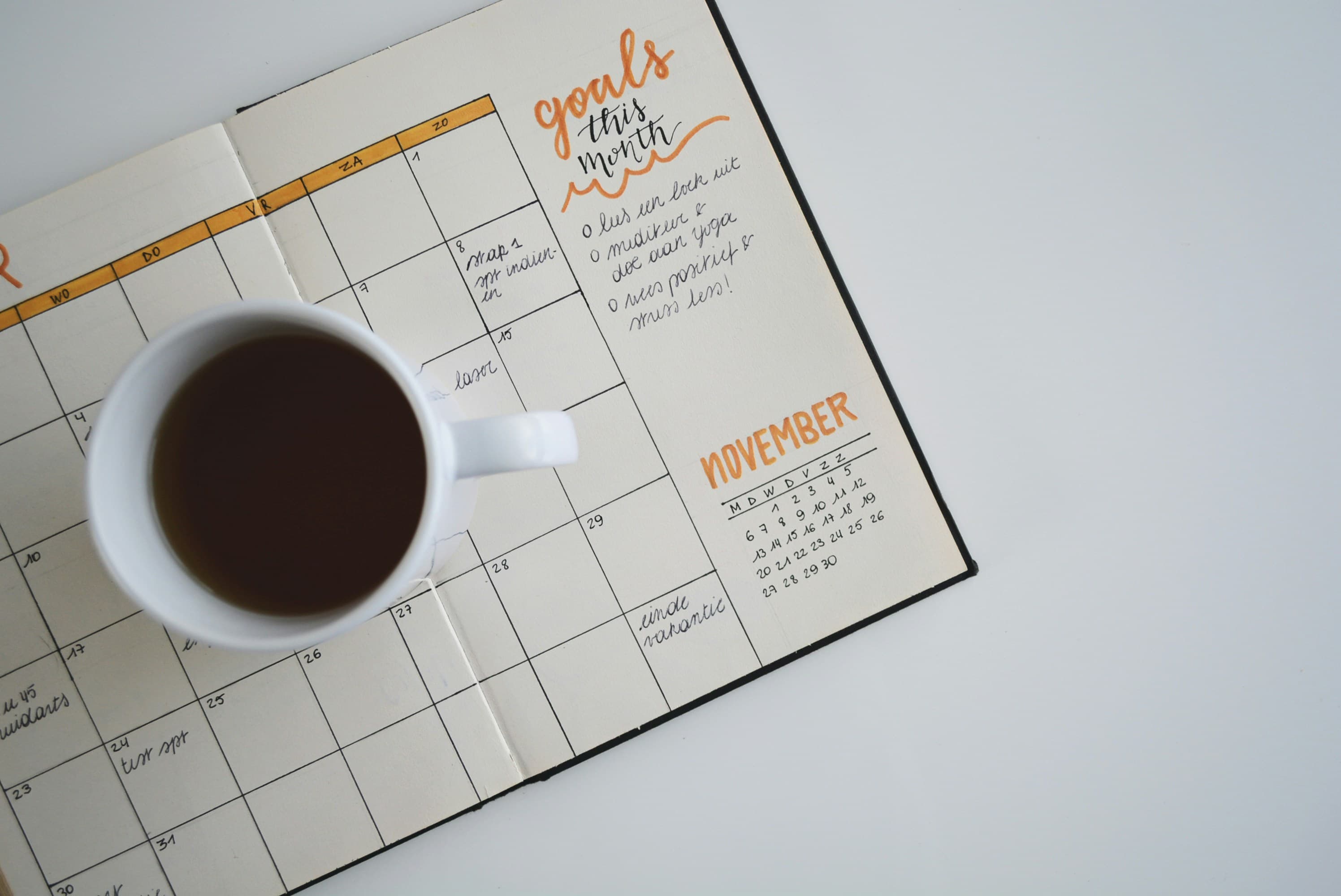 An open monthly planner with a handwritten 'goals this month' list and a cup of coffee, the kind of scheduling a German-to-B1 plan actually needs