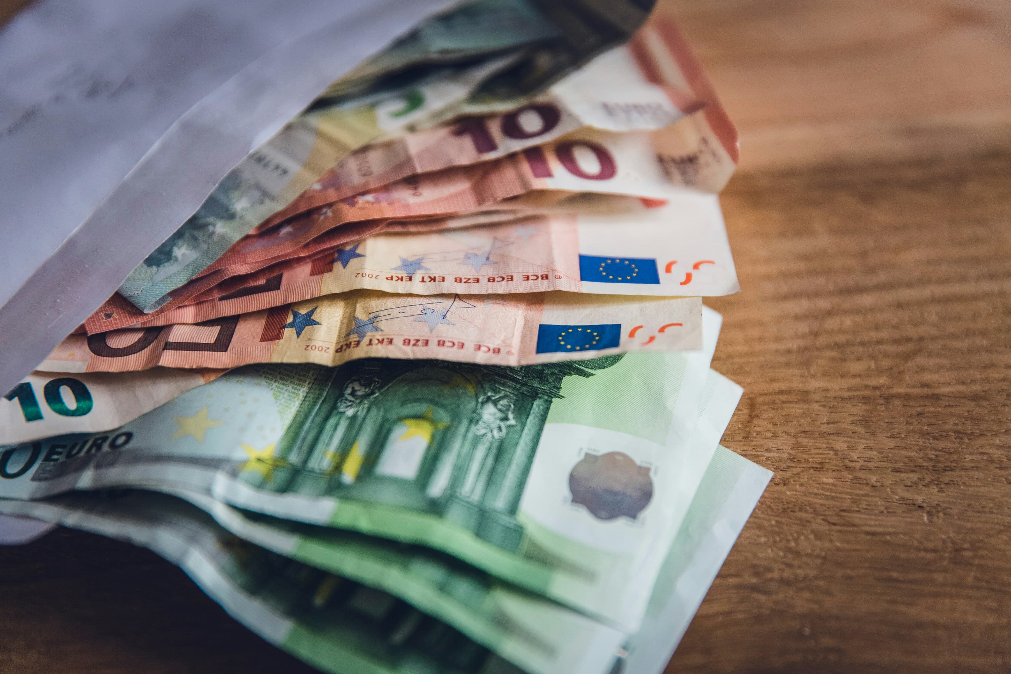 Euro banknotes spread across a wooden surface, representing the cost of sitting a German language exam