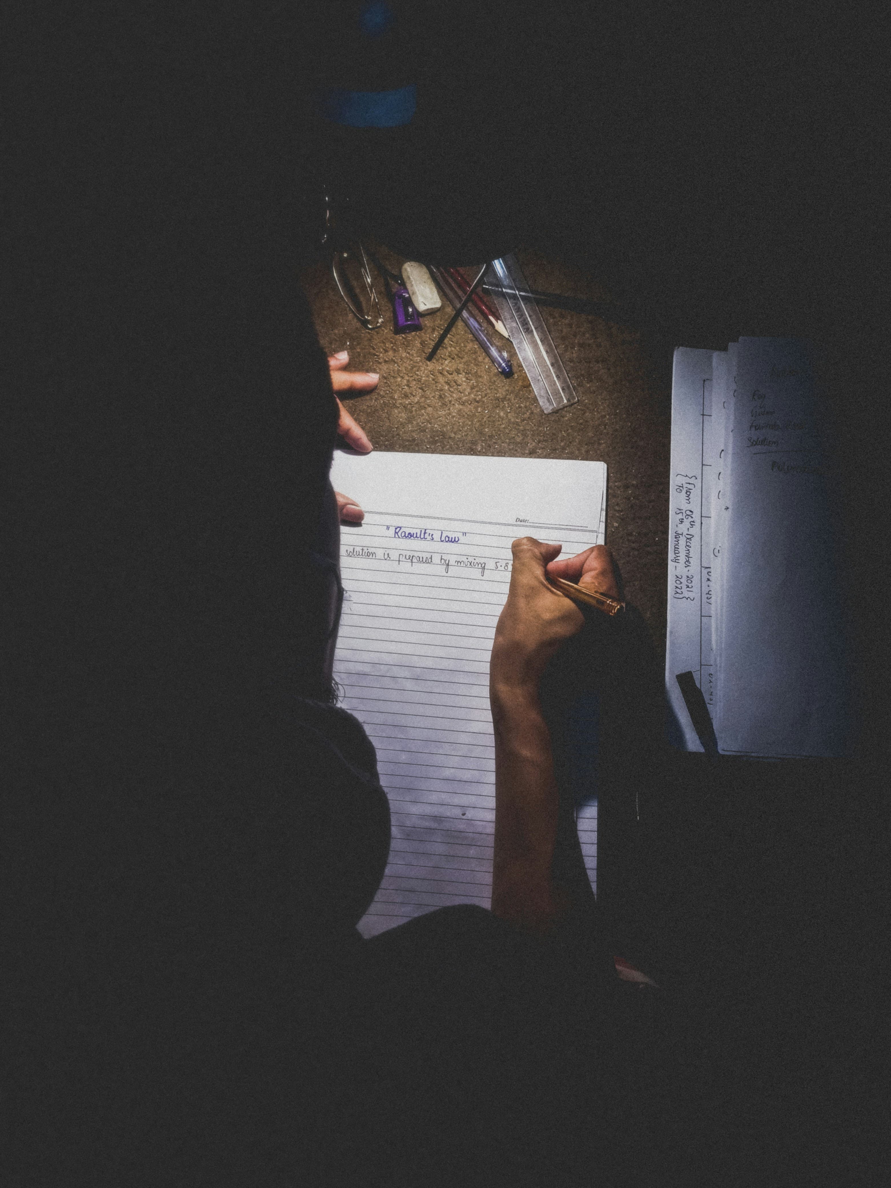 A person at a desk writing on a sheet of paper, preparing to retake a German language exam
