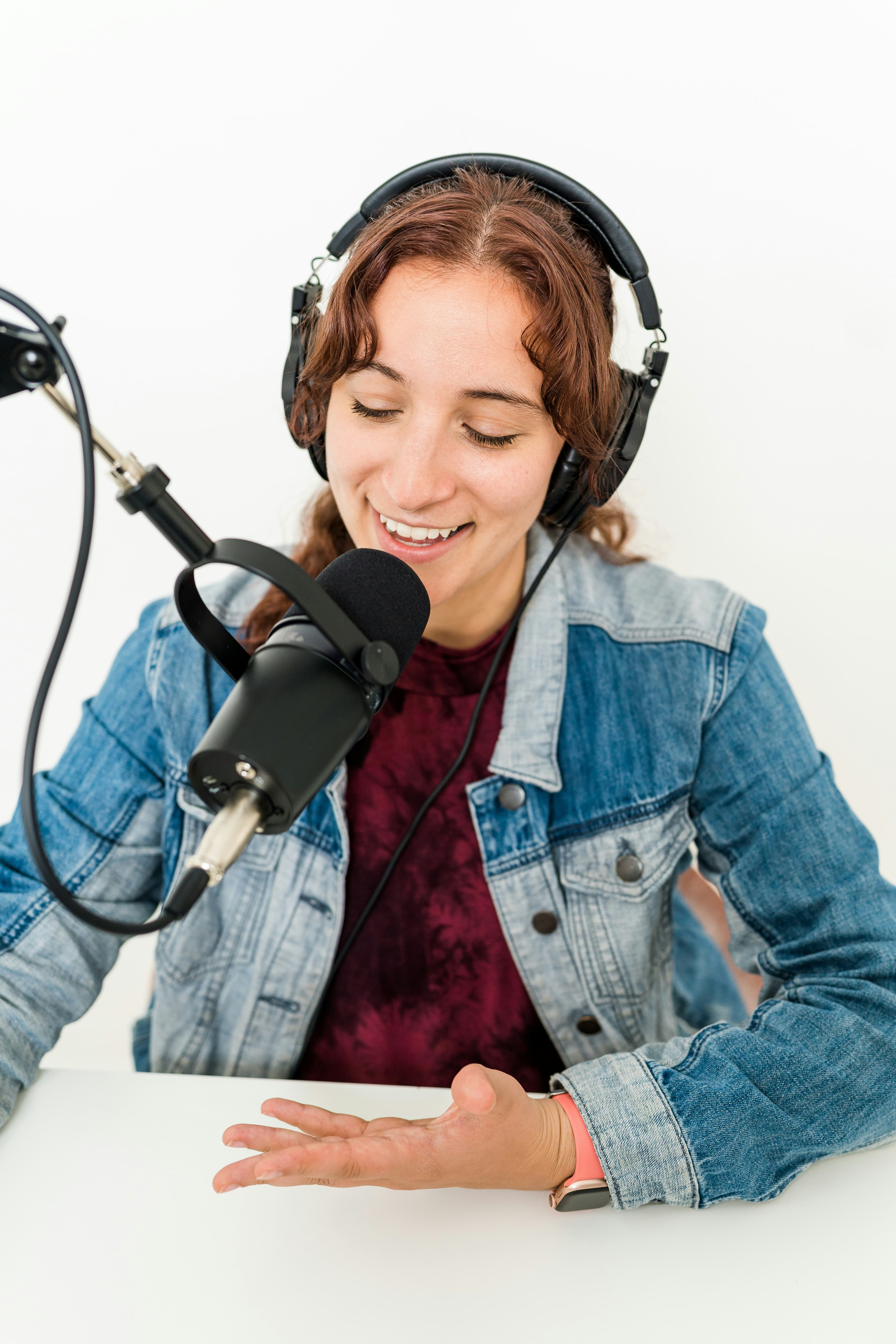 A person wearing headphones and smiling while speaking into a microphone, recording a podcast episode