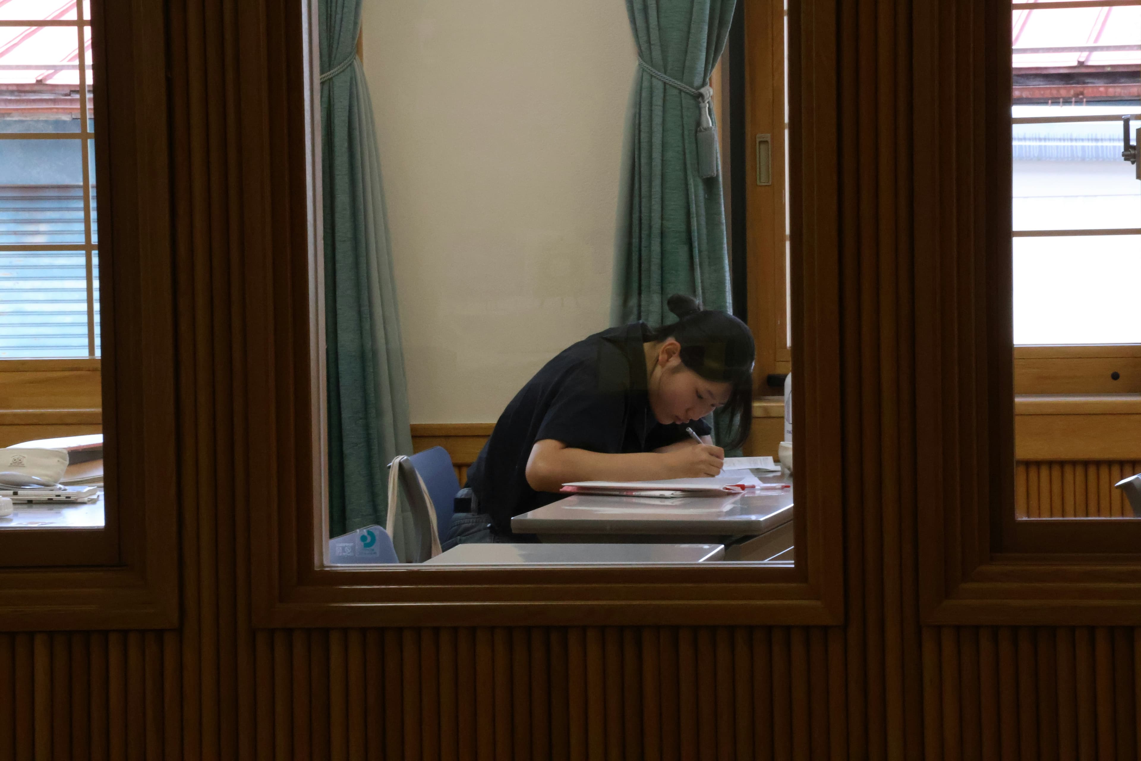 A person studying at a library desk with open books and handwritten notes, preparing for a B1 German exam