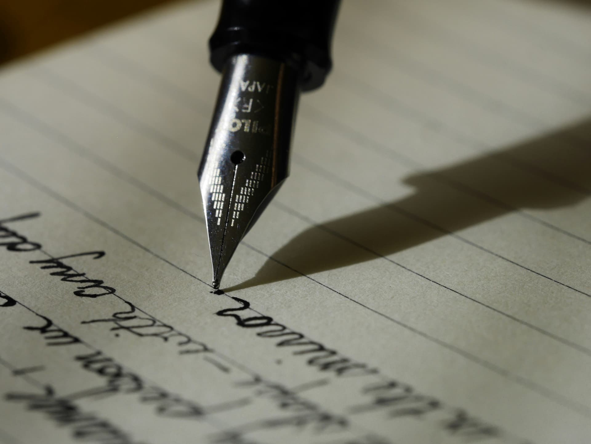 A hand writing with a fountain pen on paper, the kind of careful drafting a formal German letter asks for