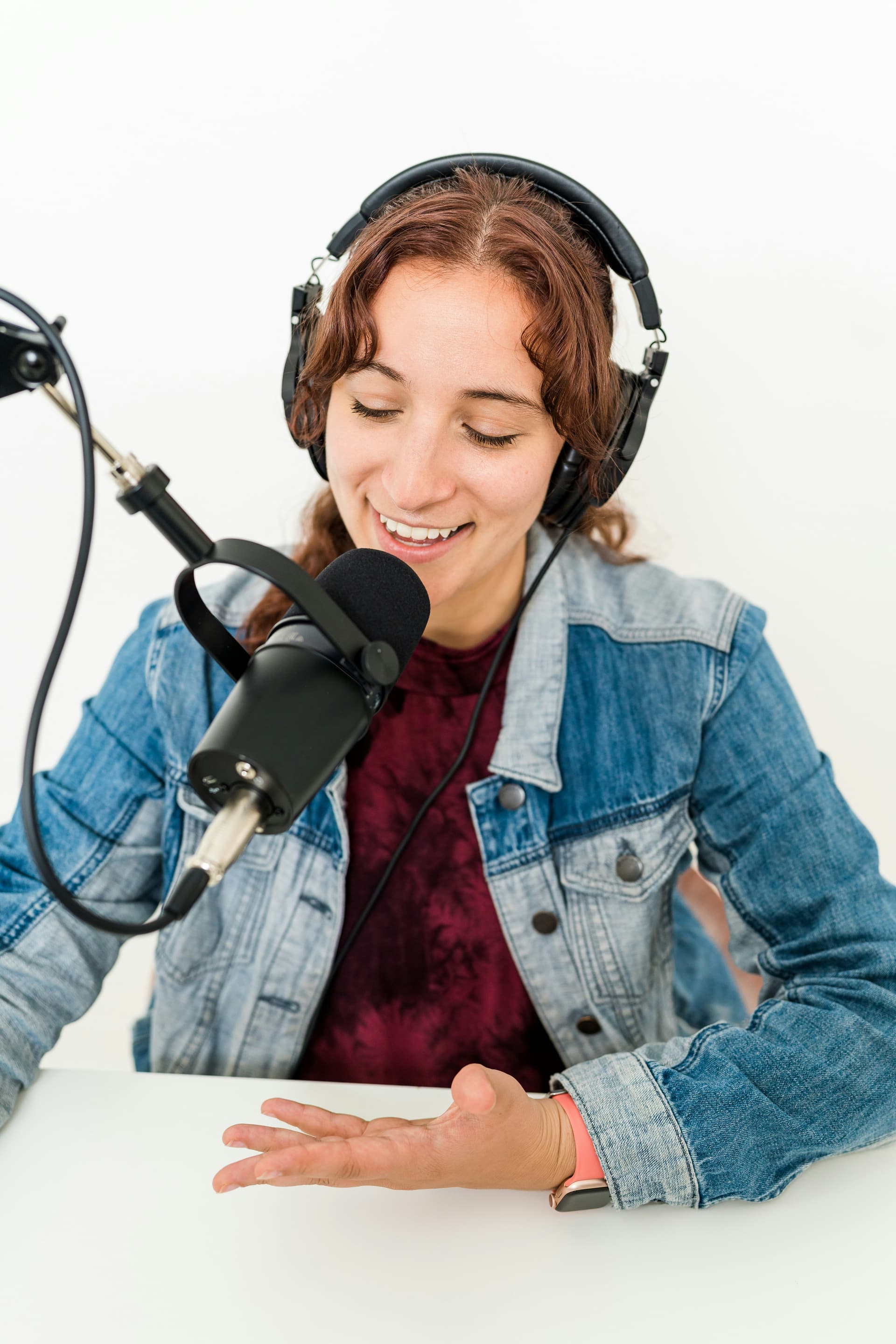 A person wearing headphones and smiling while speaking into a microphone, recording a podcast episode